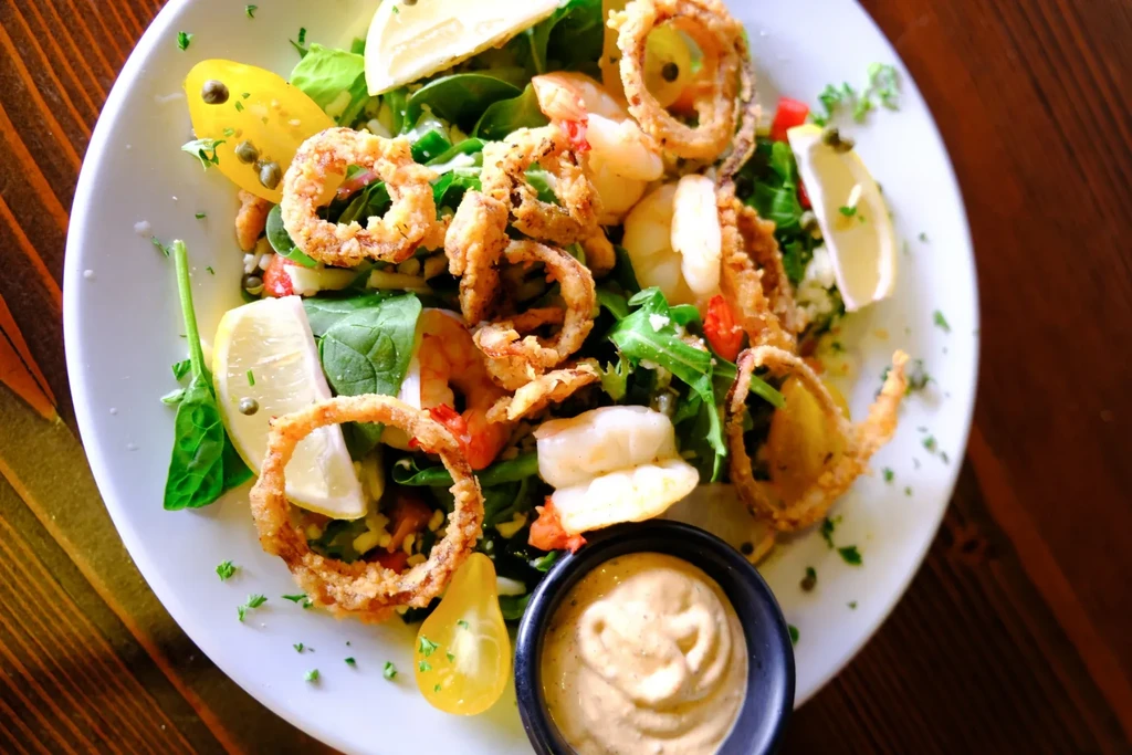 Close-up seafood salad: fried calamari, shrimp, greens, tomatoes, sauce.
