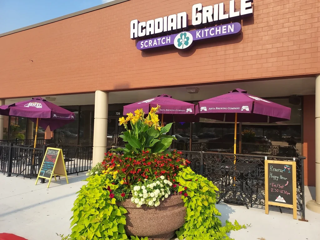 Acadian Grille restaurant's brick exterior, patio, purple umbrellas, and flower planter.