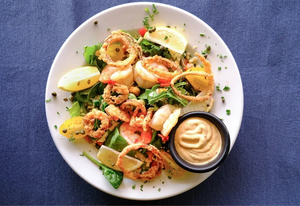 Overhead shot of shrimp and calamari salad with greens and sauce.