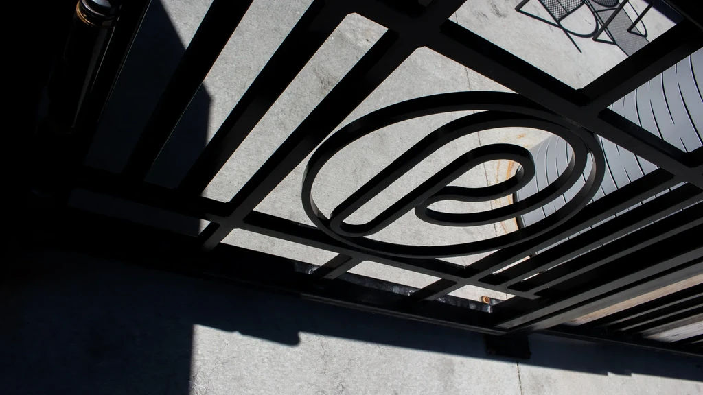 Abstract view of dark metal grate with central swirl design and shadows.