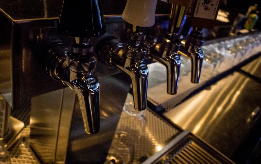 Shiny chrome beer taps with black and white handles behind a bar.