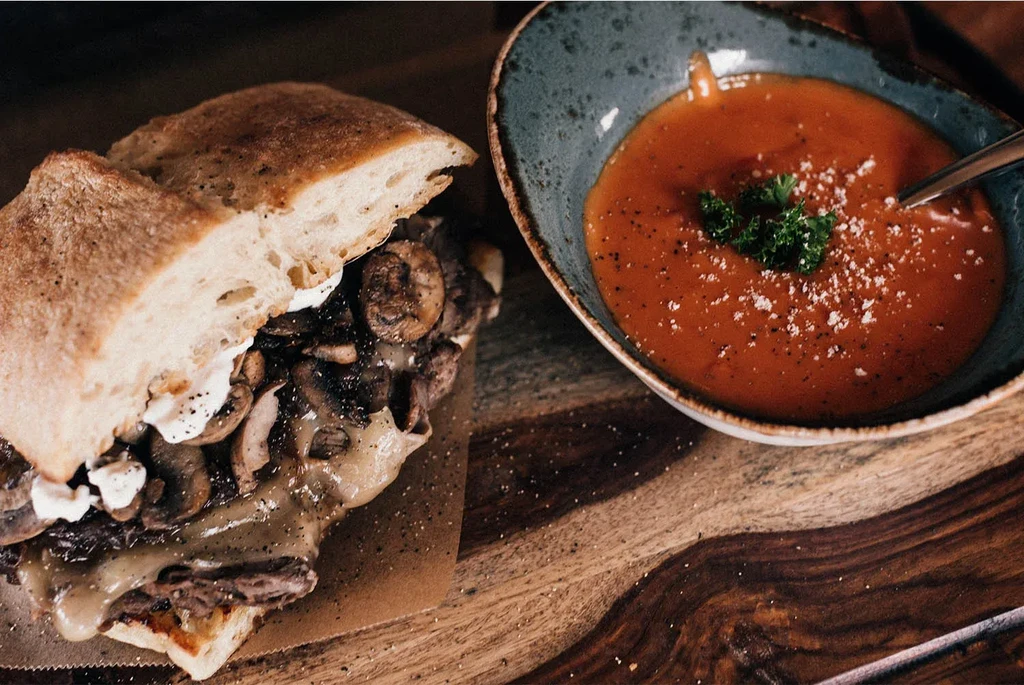 Overhead view: Halved sandwich and red soup on a dark wood table.