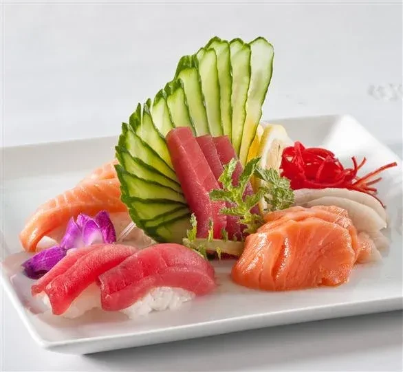 Rectangular white plate with assorted sushi, sashimi, and decorative garnishes.