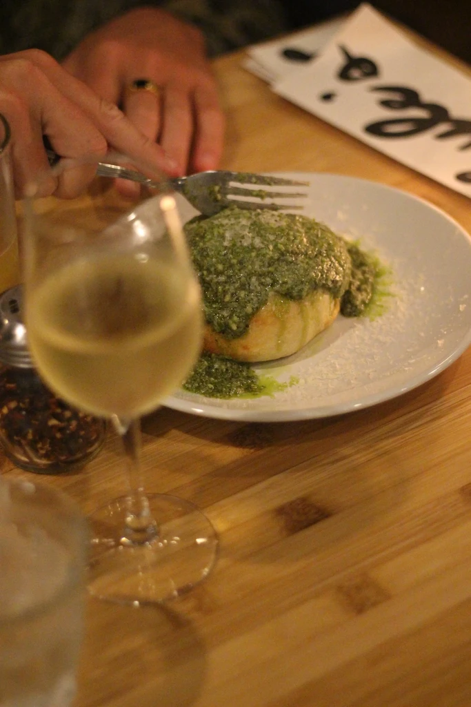 Hands cutting pesto-covered bread with cheese at a restaurant.
