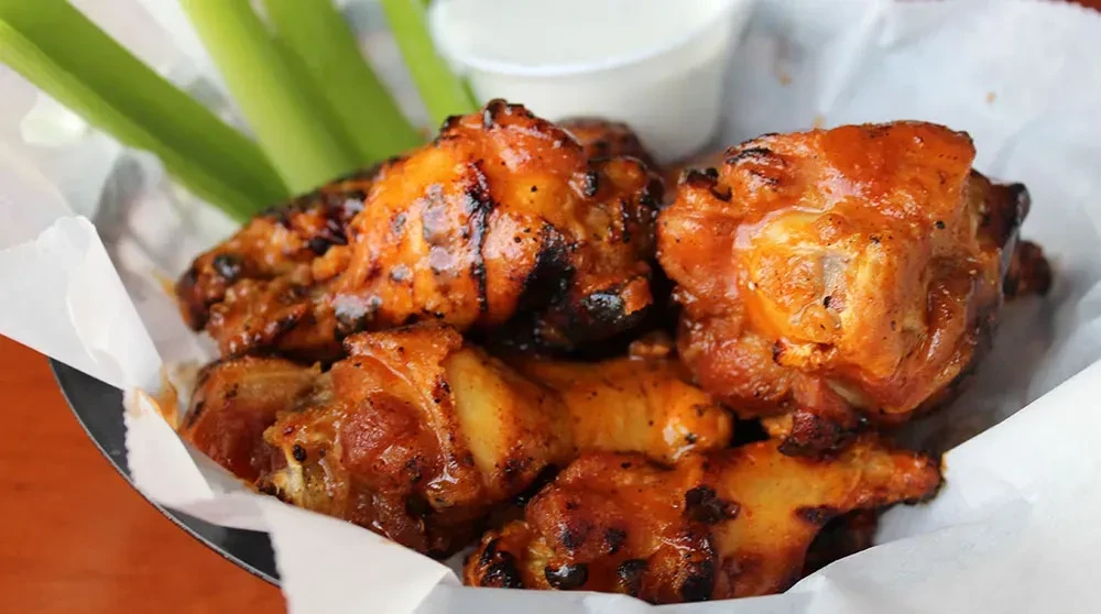 Top-down of char-marked chicken wings, celery sticks, and creamy dip.