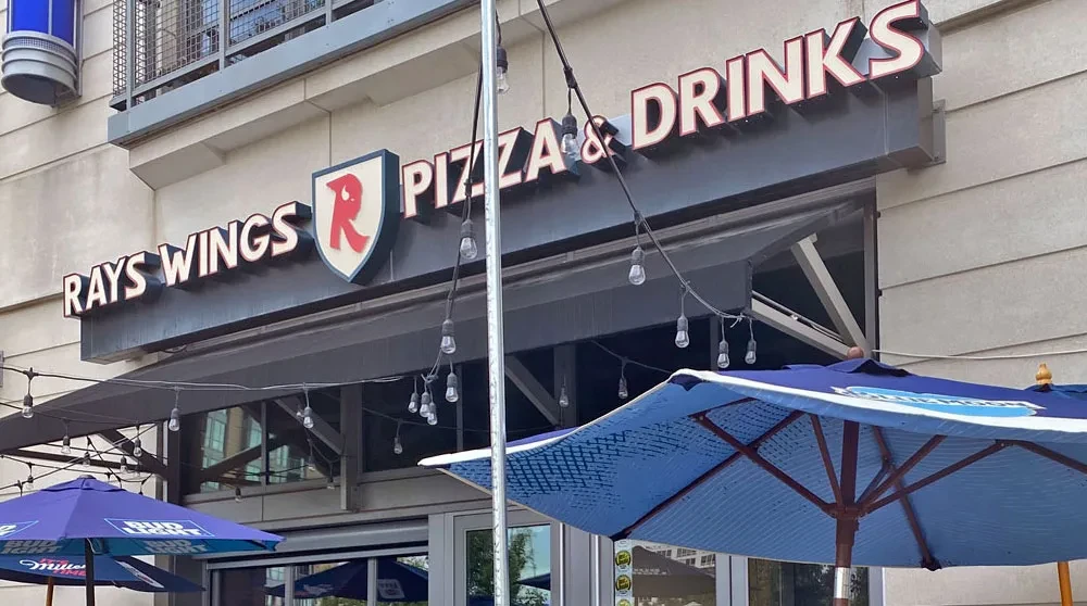 Rays Wings Pizza & Drinks storefront with illuminated sign, umbrellas, and string lights.