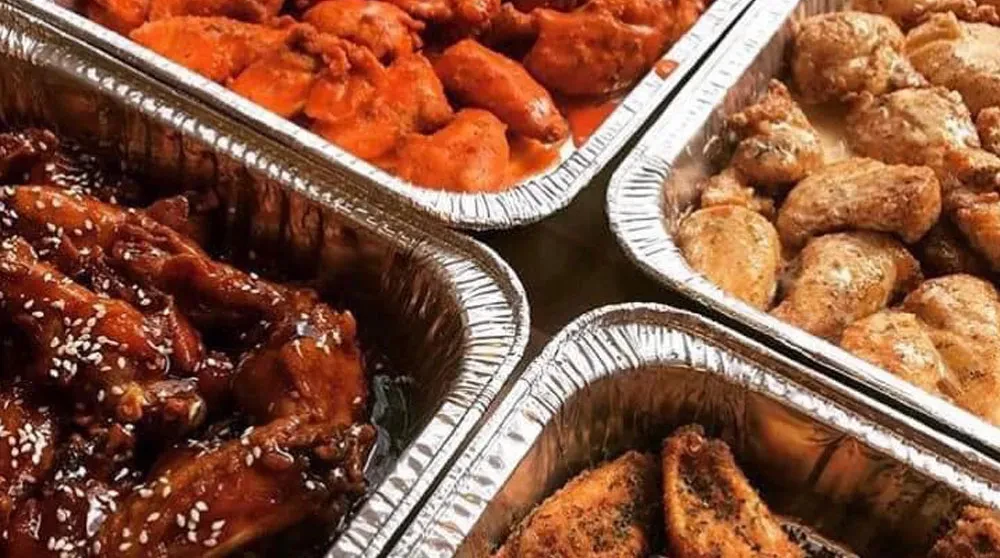 Overhead view of four foil pans filled with various cooked chicken.