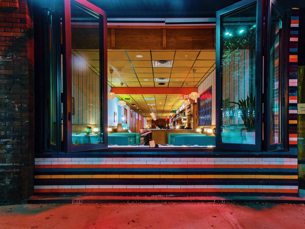 Vibrant restaurant entrance at night with colorful striped tiles, bright retro interior.