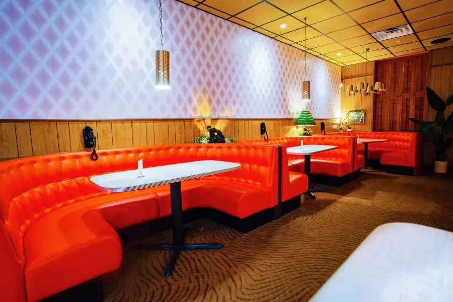 Empty retro diner: vibrant orange booths, white tables, wood paneling.