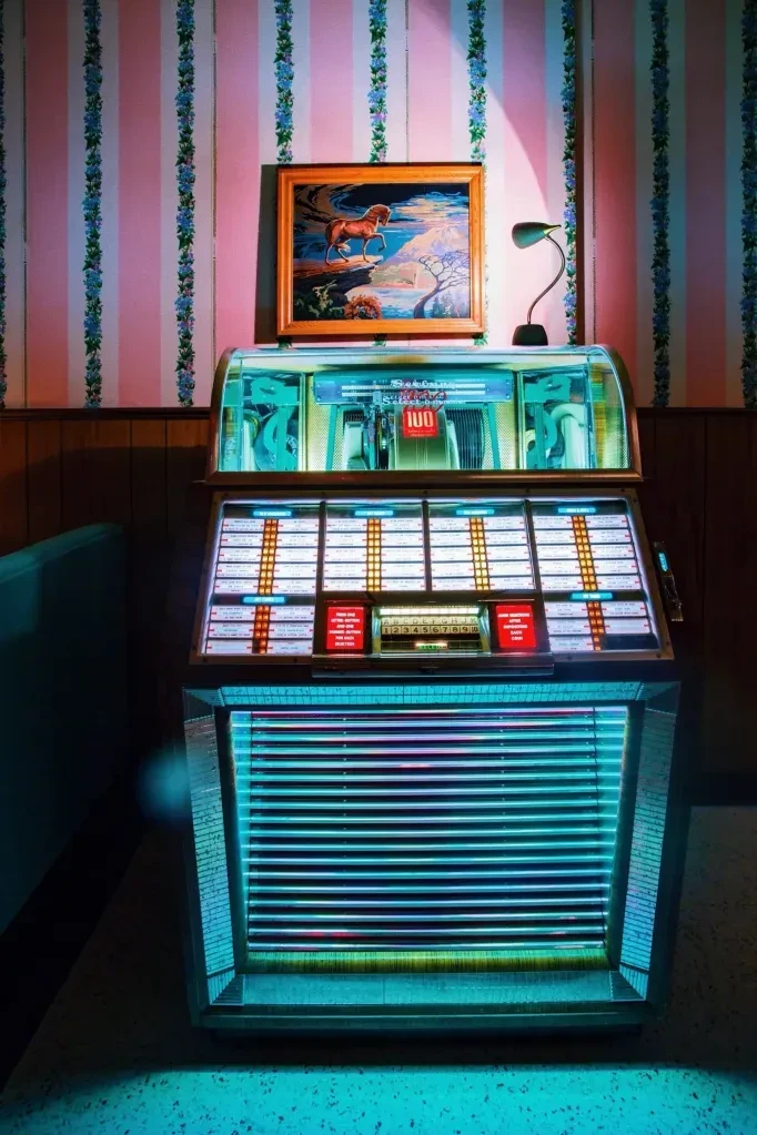 Vintage jukebox glowing with blue-green neon, horse painting, patterned wallpaper.