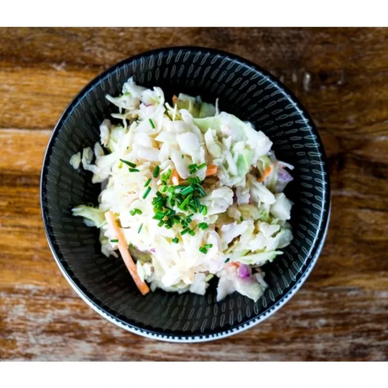 Creamy coleslaw with chives in a dark textured bowl on wood.