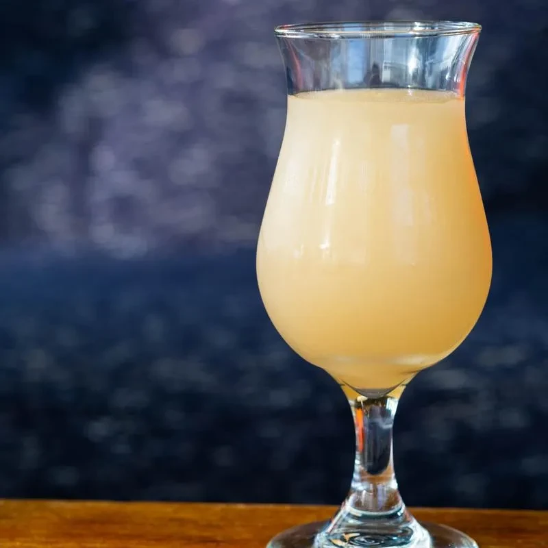 Clear goblet with light yellow beverage on a wooden surface.
