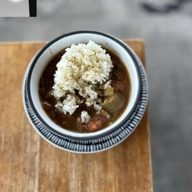 Top-down view of a dark gumbo with rice, okra, and meat.