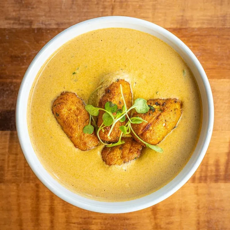 Creamy orange soup with golden fried fritters and green microgreens.