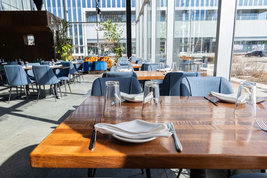 Bright modern restaurant with set tables, blue chairs, and city views.