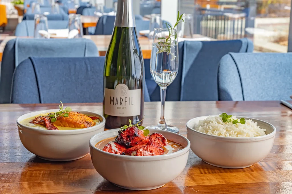 Curry, tandoori chicken, rice bowls, sparkling wine on a restaurant table.