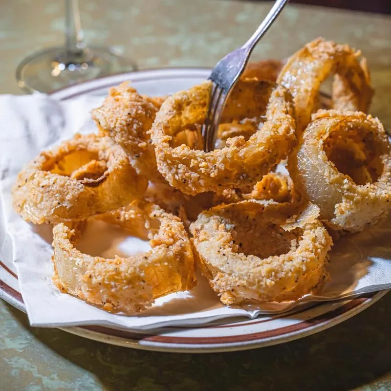 Crispy, golden-brown onion rings piled on a plate with a fork.