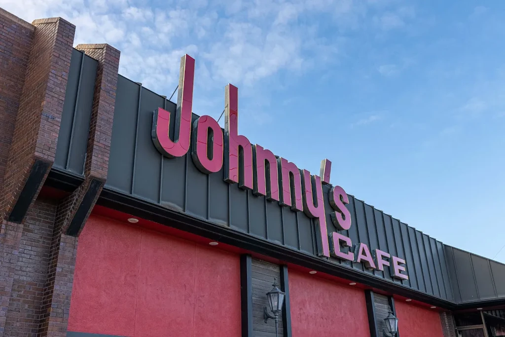 "Johnny's Cafe" sign on gray and red building, clear blue sky.