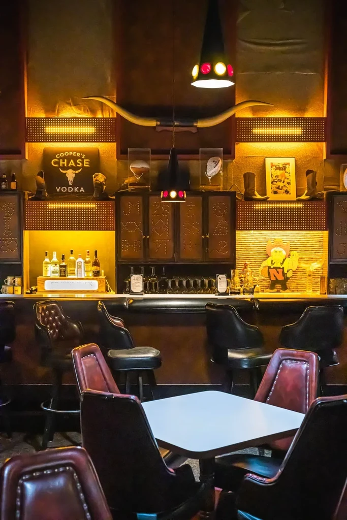 Warm, rustic bar interior with longhorn horns, liquor, and leather stools.