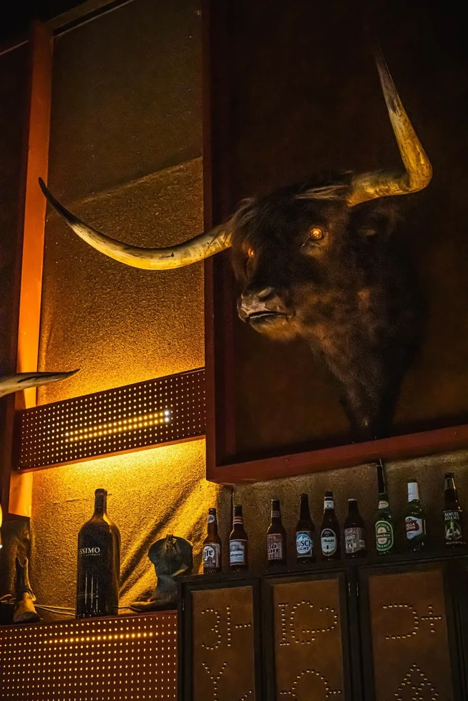 Large taxidermied bull's head with glowing orange eyes in rustic bar.