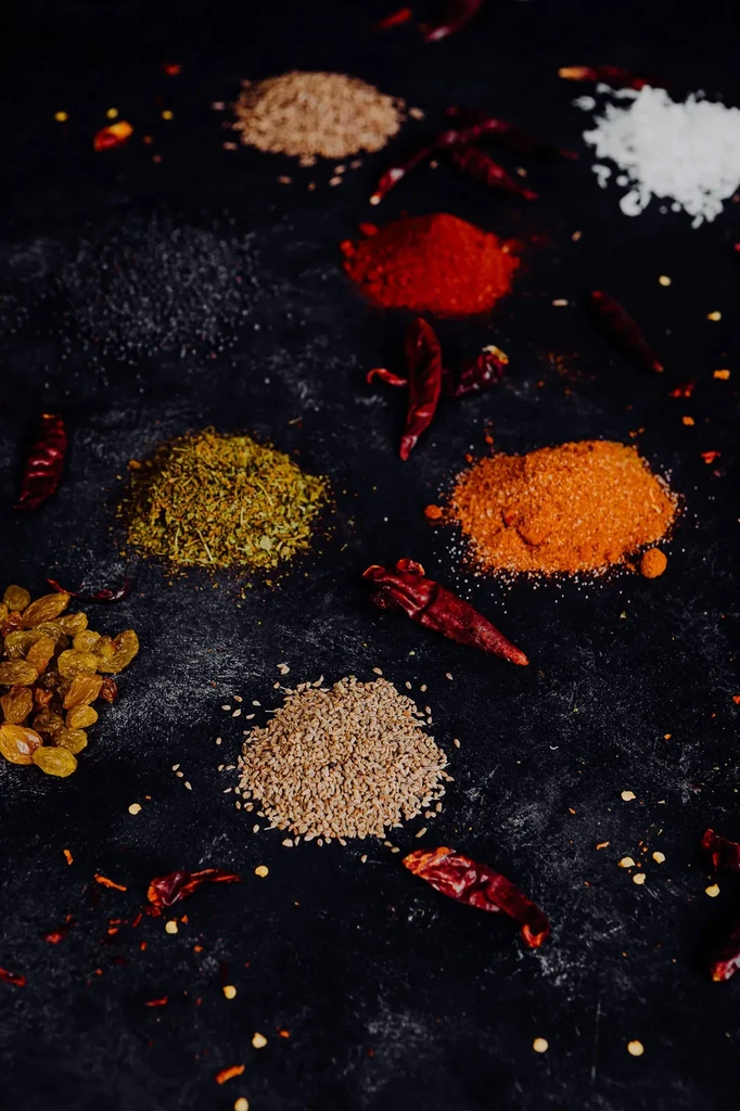 Overhead shot of colorful spices, herbs, and raisins on a dark surface.