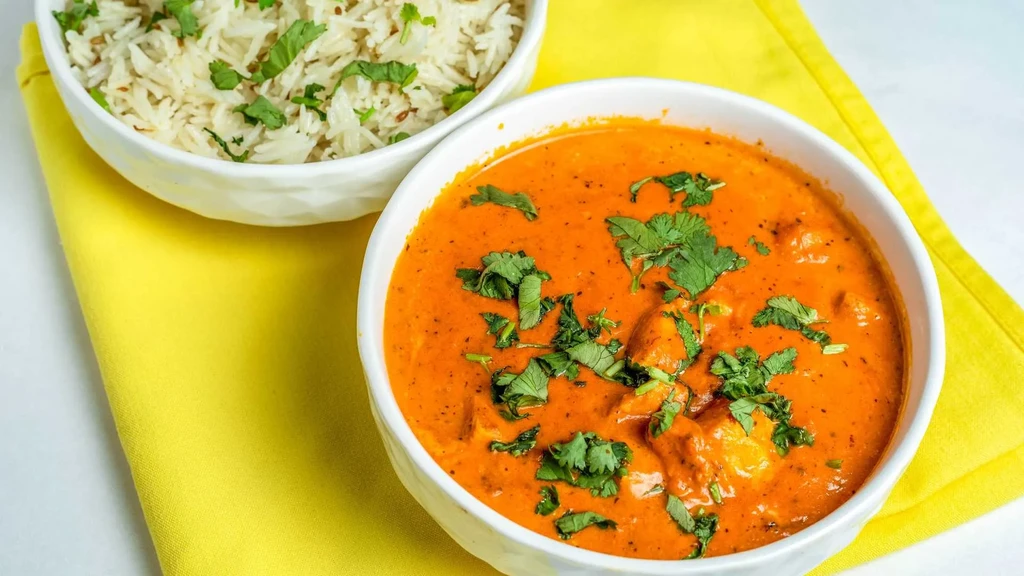 Orange-red curry and white rice in bowls on a yellow napkin.