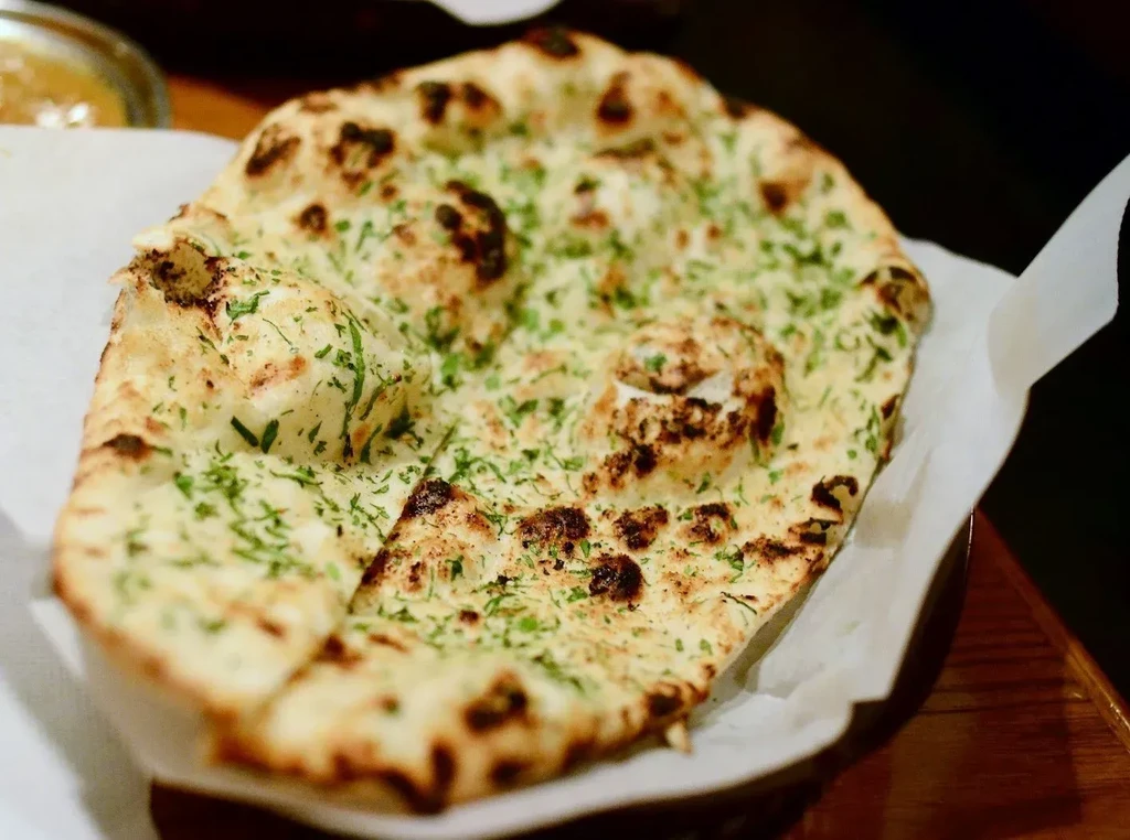 Golden-brown naan bread, bubbly and charred, topped with green herbs.