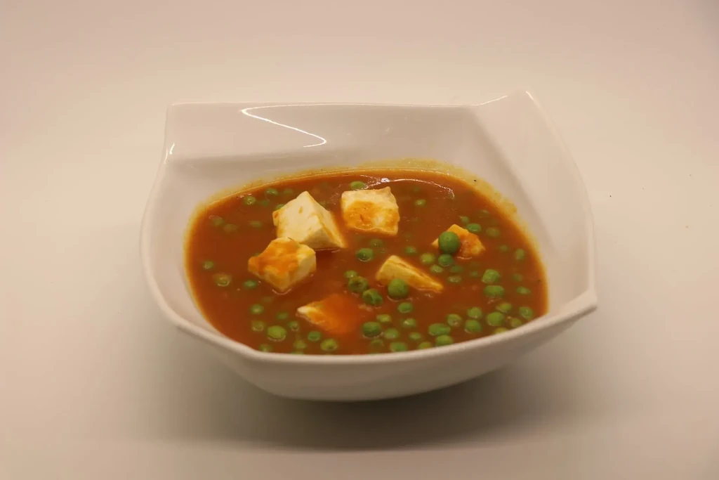 Indian paneer and peas curry in a white bowl with a wavy rim.