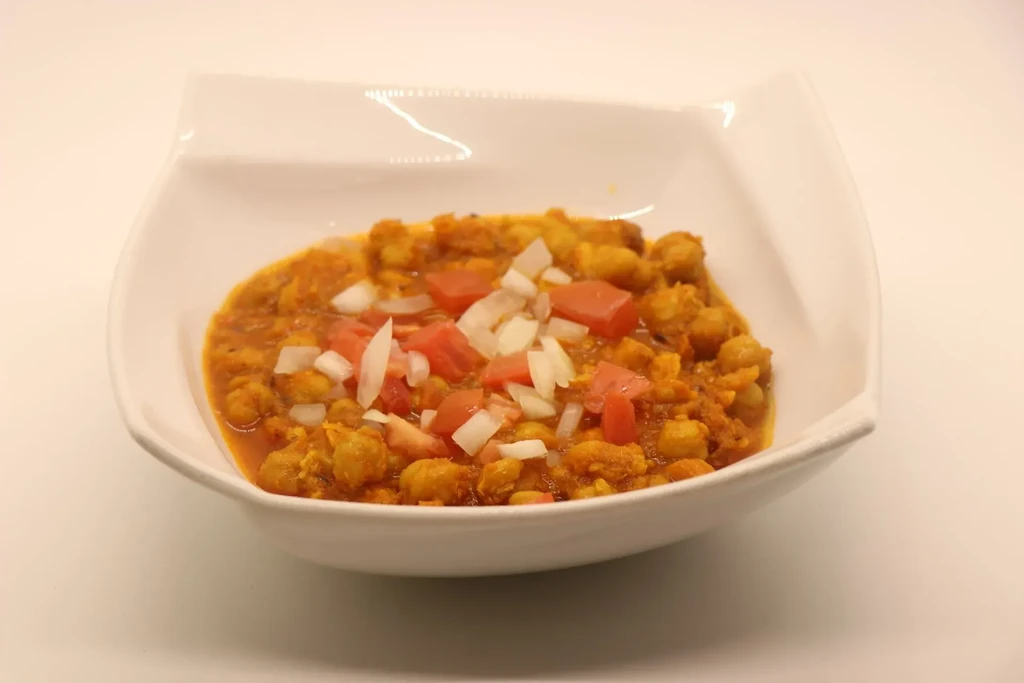 Chickpea curry in a white bowl, garnished with tomatoes and onions.