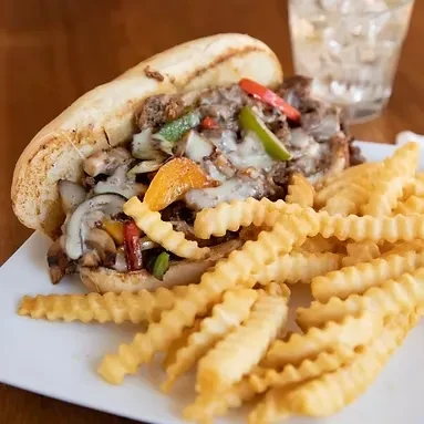 Cheesesteak sandwich with melted cheese, peppers, mushrooms, and crinkle fries.