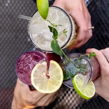 Overhead, hands hold three colorful, garnished drinks for a toast.