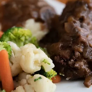 Braised meat with gravy and mixed vegetables on a white plate.