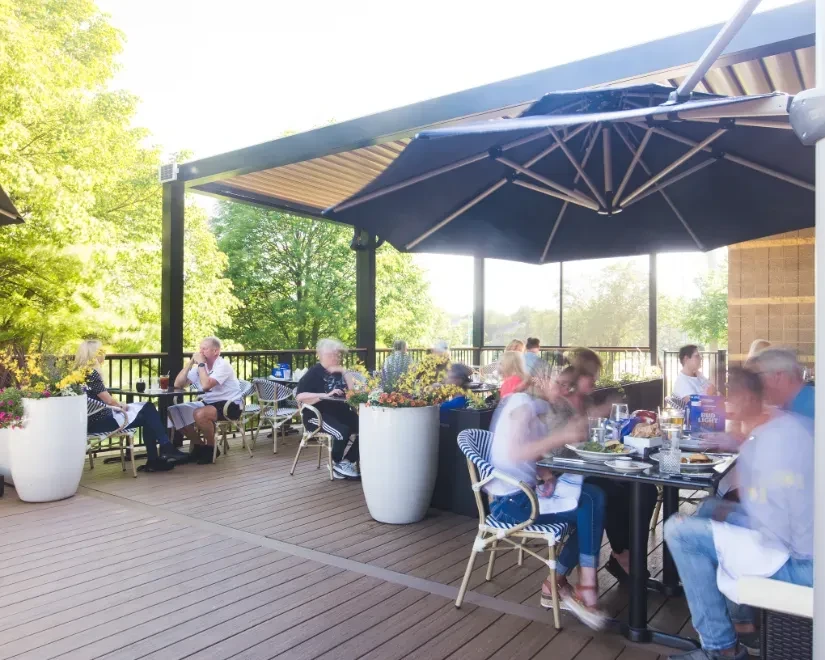 Outdoor restaurant patio with dining groups, shade structures, and potted flowers.