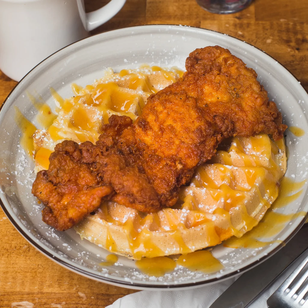 Crispy fried chicken and waffles, drizzled with syrup and sugar.
