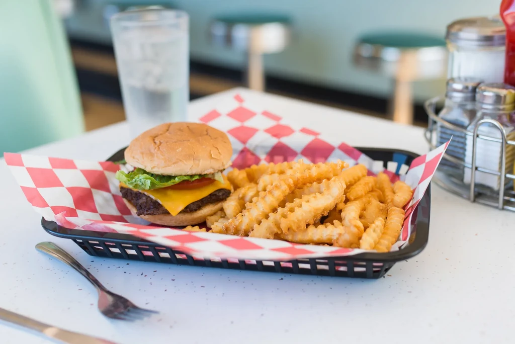 Cheeseburger and waffle fries in a basket with condiments, diner setting.