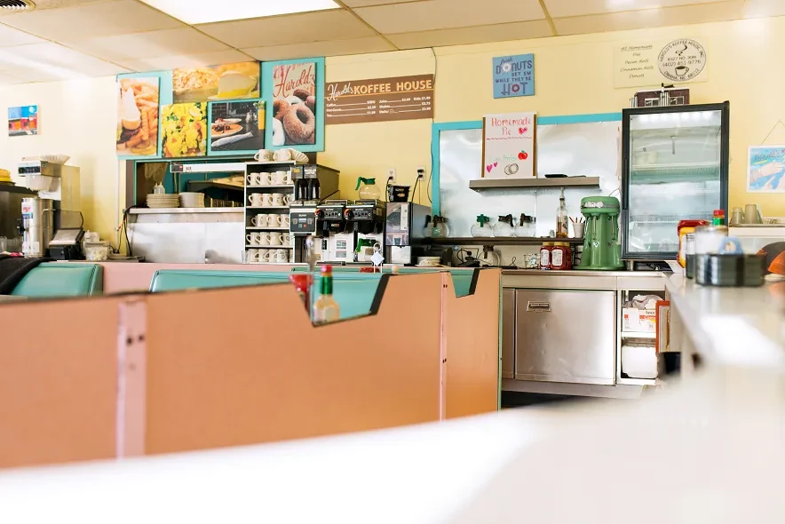 Vintage diner counter and booths, with coffee machines and food posters.