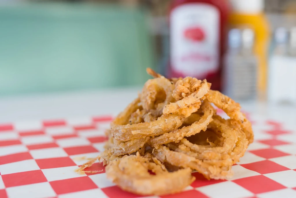 Golden-brown onion rings piled on checkered paper with blurred condiments.