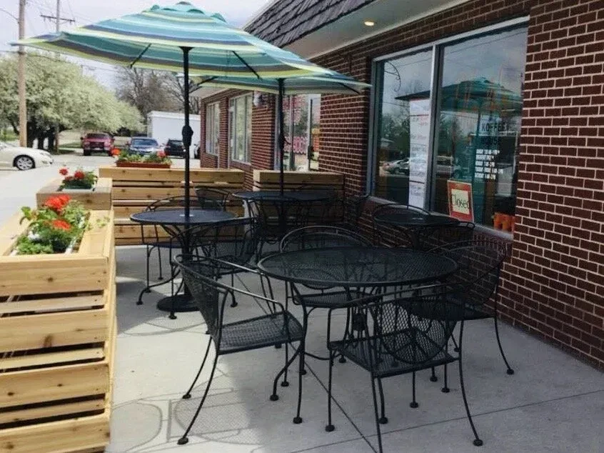 Outdoor cafe patio with black tables, striped umbrellas, and vibrant flowers.