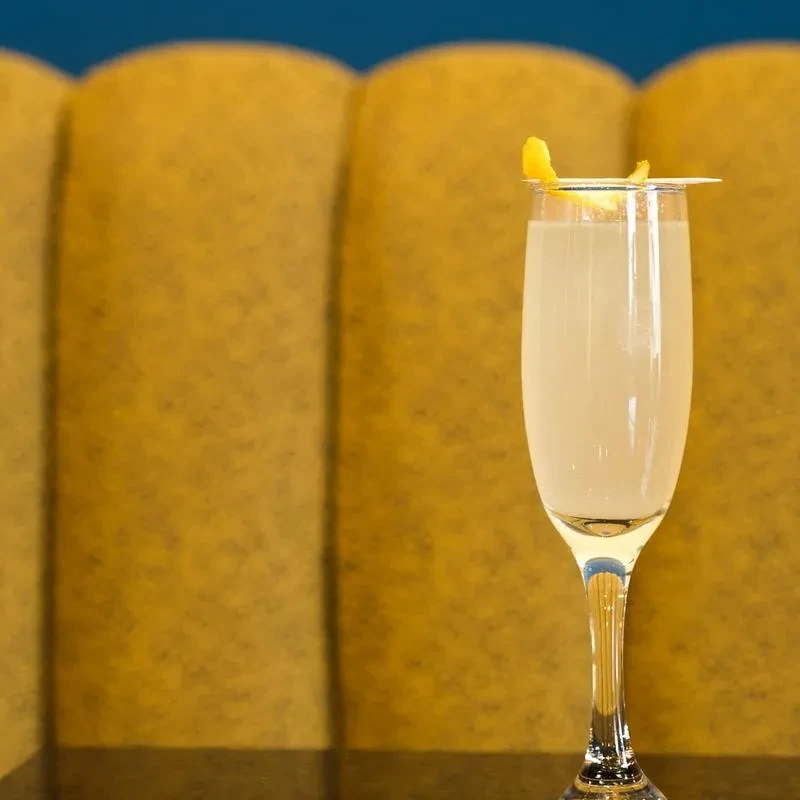 Champagne flute with a light cocktail, lemon twist, yellow scalloped paneling.