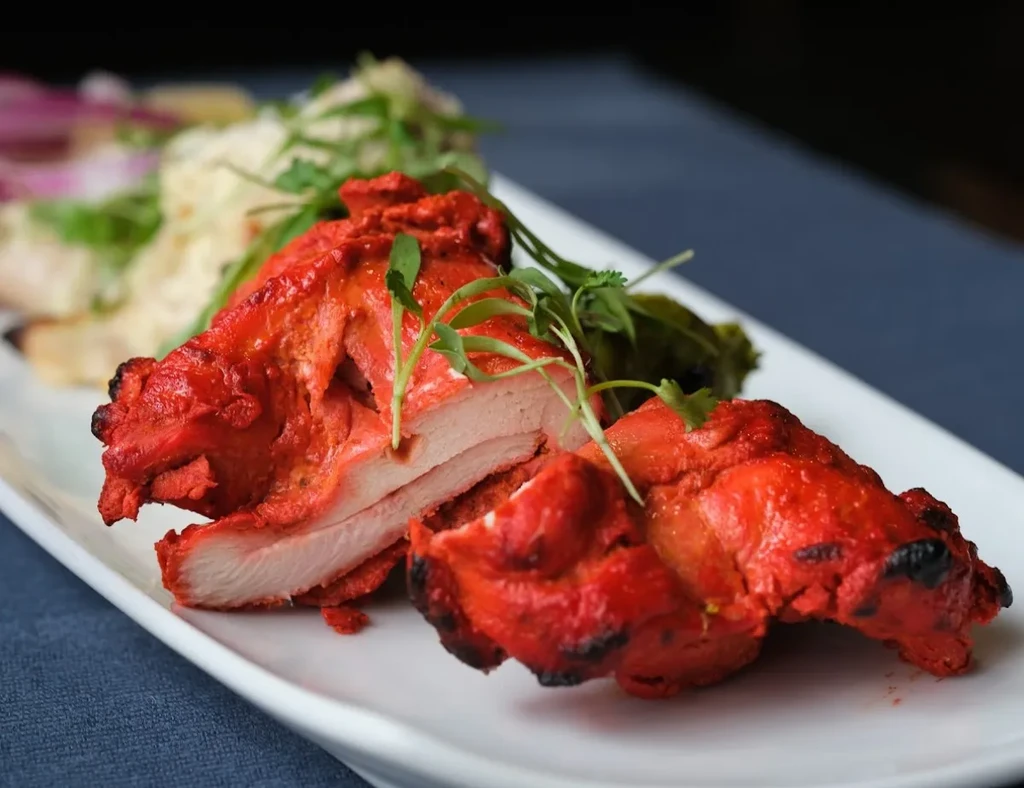 Close-up of red-orange tandoori chicken garnished with green herbs.