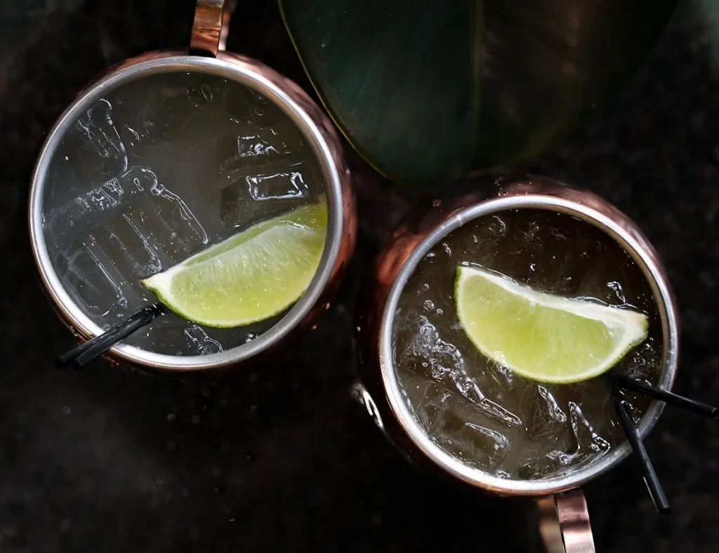 Two copper Moscow Mule mugs with ice, lime, and straws.