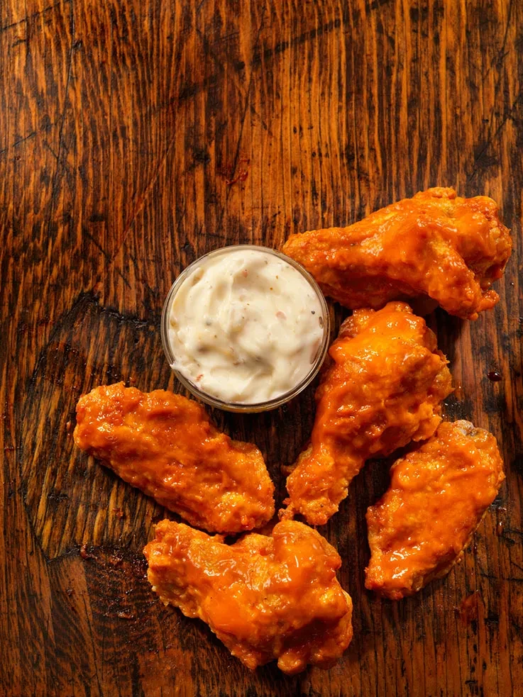 Five buffalo wings and dipping sauce on rustic wood.