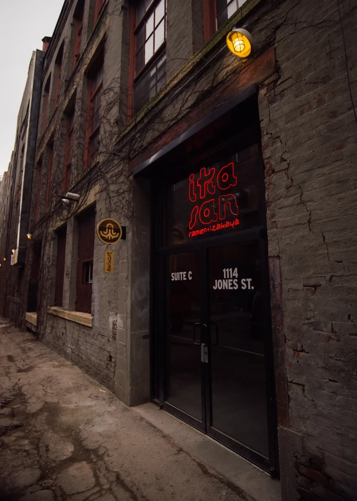 Entrance to Ika San Ramen+Izakaya in a gritty brick building alley.