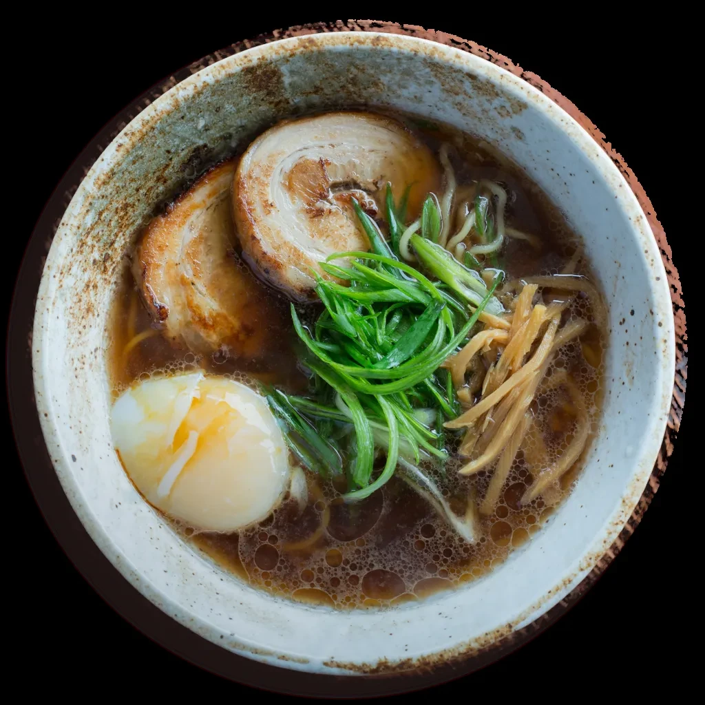 Ramen bowl with chashu, egg, scallions, bamboo, and dark broth.