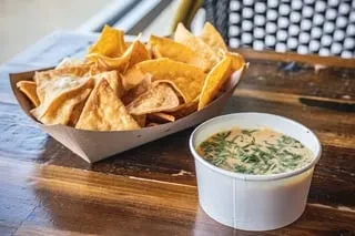 Golden tortilla chips in boat with creamy green chili dip.