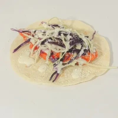 Taco with reddish protein, purple cabbage, slaw, creamy sauce, and cheese.