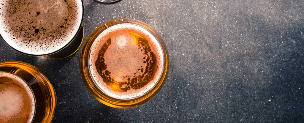 Overhead view of three golden beers with foamy heads on dark stone.