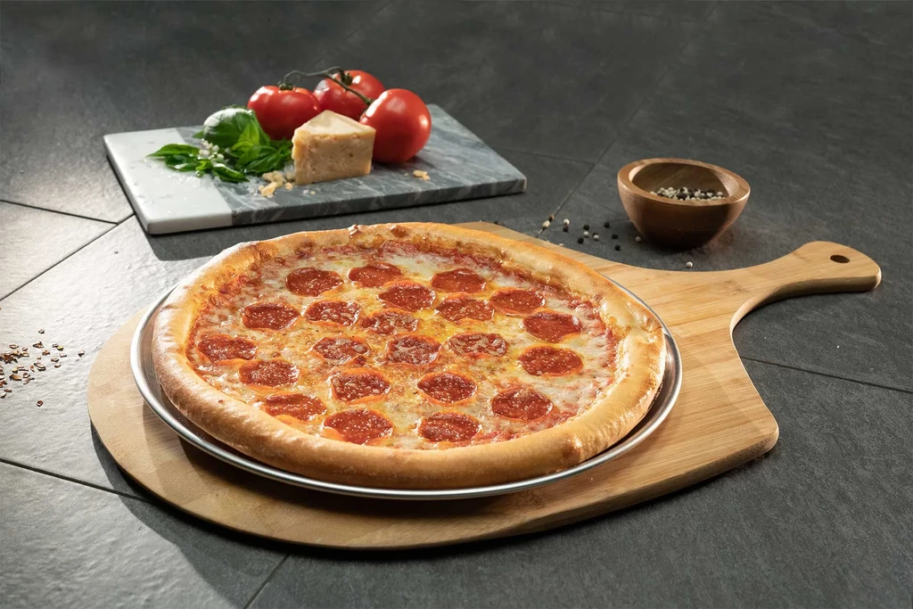 Freshly baked pepperoni pizza on a peel with tomatoes, basil, and cheese.