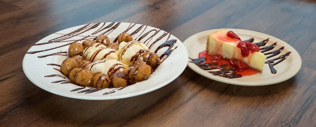 Fried dough balls with ice cream next to strawberry cheesecake.