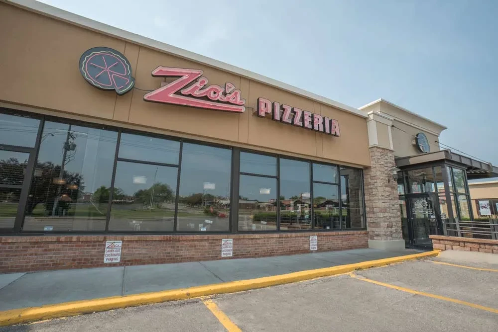 Exterior of Zio's Pizzeria showing its red sign, windows, and brick facade.